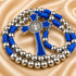 A silver beaded rosary with a blue cord and cross, on a beige satin fabric background.