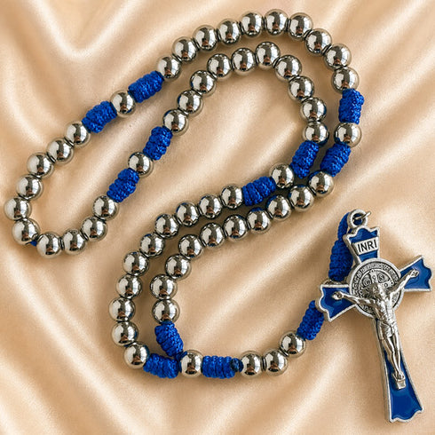 A rosary with metal beads, blue knotted cord, and a matching blue and silver crucifix pendant, on satin background.