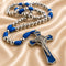 A blue and silver beaded rosary with a crucifix, displayed on a draped beige satin fabric background.