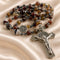 A beaded rosary with brown agate beads, a silver St Benedict medallion, and a silver crucifix, on a draped champagne satin fabric.