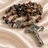 A beaded rosary with brown agate beads, a silver St Benedict medallion, and a silver crucifix, on a draped champagne satin fabric.