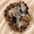 A rosary with brown agate beads, dark metallic spacer beads, a silver-toned crucifix, and a small round saint medal.