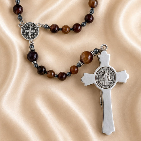 A rosary with brown and dark beads, a silver-tone crucifix and a round medallion, displayed on a beige satin fabric.