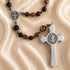 A rosary with brown and dark beads, a silver-tone crucifix and a round medallion, displayed on a beige satin fabric.