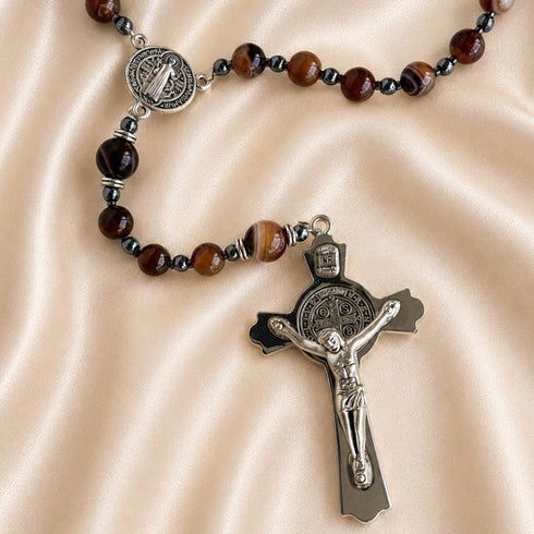A rosary featuring amber marbled beads, silver-tone St Benedict medallion, and a detailed silver crucifix pendant.