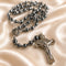 Hematite rosary with St Benedict medallion, and a silver-toned crucifix, on a cream satin fabric background.