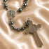 A rosary with dark hematite beads and a silver-tone cross pendant with a St Benedict medallion, on a champagne satin fabric.