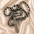 A hematite rosary with a silver-toned cross pendant and a round medallion, arranged on a satin fabric background.