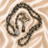A rosary with hematite beads, a silver-toned crucifix, and a small round St Benedict medal, on a satin fabric background.