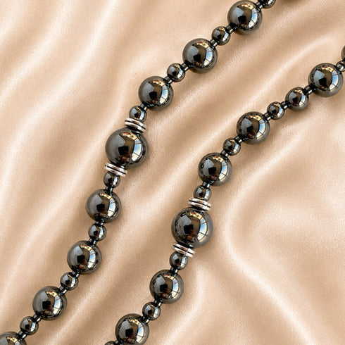 A close-up of a hematite rosary with large and small polished round beads separated by small silver spacer rings.