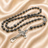 A black hematite rosary with a silver-tone crucifix and St Benedict medallion, on a beige satin fabric.