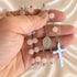 Pink jade rosary held in hand: St. Benedict medal and silver cross