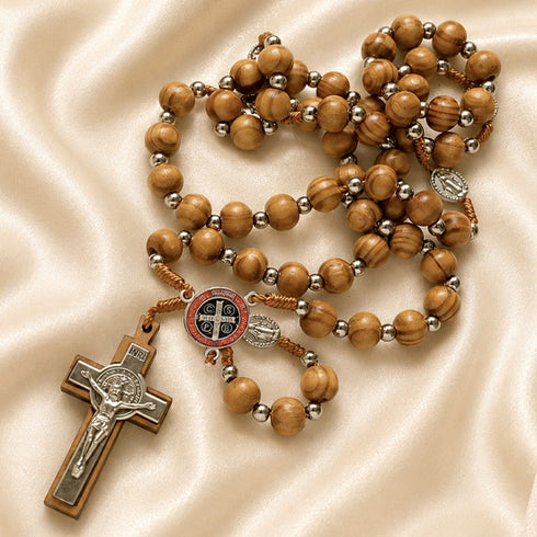 Olive wood rosary with St. Benedict medal centerpiece and silver crucifix on satin cloth background.
