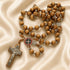 Olive wood rosary with St. Benedict medal centerpiece and silver crucifix on satin cloth background.