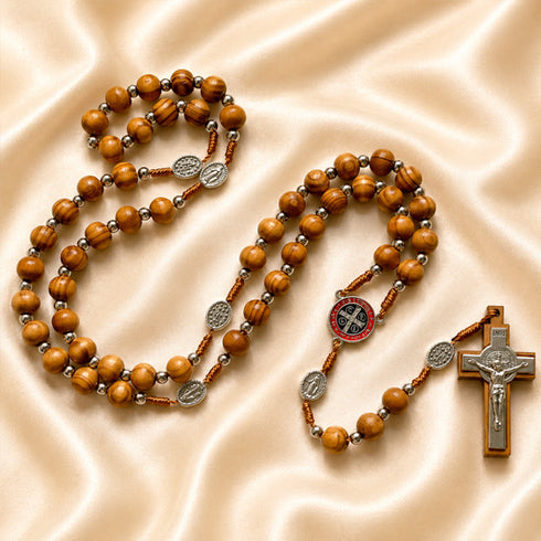 Olive wood rosary with St. Benedict medal centerpiece and silver crucifix on satin cloth background.