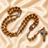 Olive wood rosary with St. Benedict medal centerpiece and silver crucifix on satin cloth background.