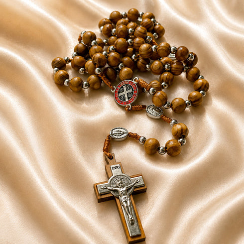 Olive wood rosary with St. Benedict medal centerpiece and silver crucifix on satin cloth background.
