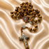 Olive wood rosary with St. Benedict medal centerpiece and silver crucifix on satin cloth background.
