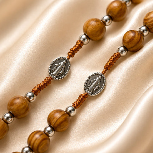 Olive wood rosary beads with Miraculous Medal markers on a folded satin beige cloth.
