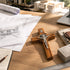 Wooden cross on a desk with architectural drawings and a laptop in the background