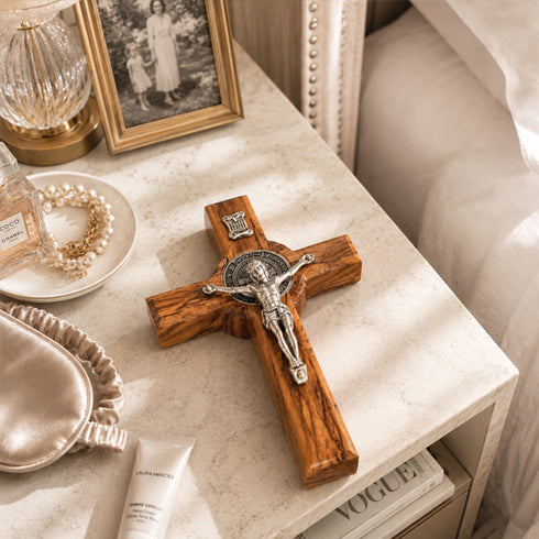 Wooden cross with silver figure on a marble surface next to a photo frame and decorative items.