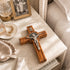 Wooden cross with silver figure on a marble surface next to a photo frame and decorative items.