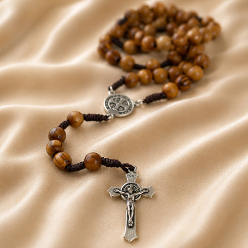 Wooden rosary with metal crucifix and a St Benedict medal centrepiece on a beige satin cloth background.