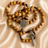 Olive wood rosary with cord and St. Benedict cross and medal, on a beige satin background.