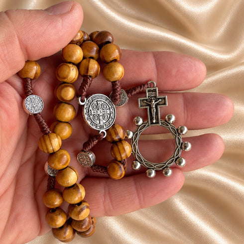 Hand holding a Saint Benedict olive wood rosary with Crown of Thorns crucifix