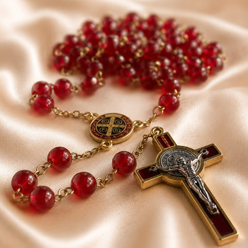 A red and gold Catholic rosary with a round St Benedict medallion, and a gold-toned crucifix with a silver-toned corpus.