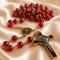 A red and gold Catholic rosary with a round St Benedict medallion, and a gold-toned crucifix with a silver-toned corpus.