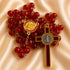 A red glass bead rosary with a gold-tone and silver-tone St Benedict cross, on a beige satin background.