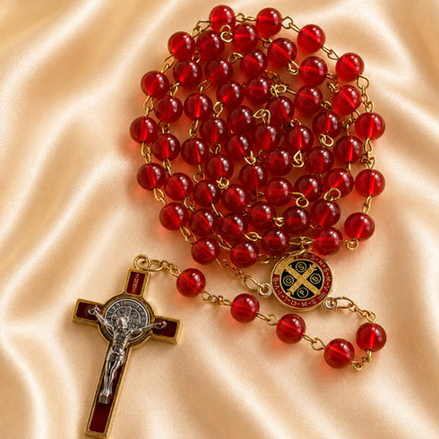 A red bead rosary with gold-tone chain links, a red-and-gold centerpiece, and a matching crucifix, on draped satin fabric.