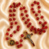 A red rosary with gold-tone chain links, a round red medallion, and a crucifix, on a satin fabric background.