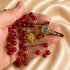 A close-up of a hand holding a red and gold rosary, a gold crucifix, and a gold medallion, on a beige satin background.