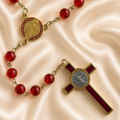A red and gold rosary laid out on a satin background, featuring red beads, a round medallion, and a cross.