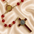 A red and gold rosary laid out on a satin background, featuring red beads, a round medallion, and a cross.