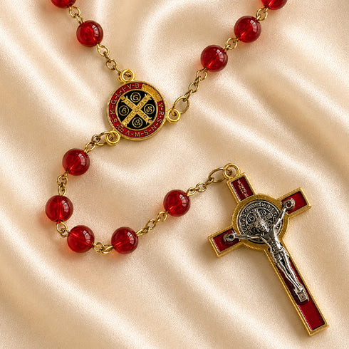 A Catholic rosary with red beads, a round centerpiece medallion, and a crucifix, on a draped satin fabric background.