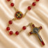 A Catholic rosary with red beads, a round centerpiece medallion, and a crucifix, on a draped satin fabric background.