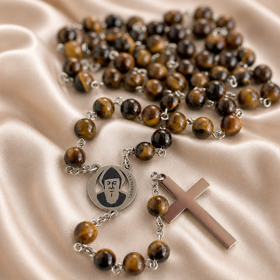 A rosary with tiger's eye beads, a round silver medal with St Charbel portrait, and a polished silver cross.