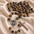 A rosary with tiger's eye beads, a round silver medal with St Charbel portrait, and a polished silver cross.