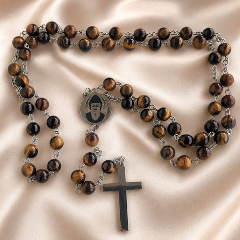 A Catholic rosary with tiger's eye beads, a round metal centerpiece, and a matte cross, on a beige satin fabric.