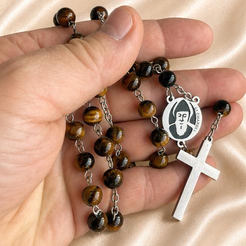 A close-up of a hand holding a Catholic rosary featuring brown tiger's eye beads, and a silver-tone cross