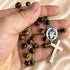 A close-up of a hand holding a Catholic rosary featuring brown tiger's eye beads, and a silver-tone cross