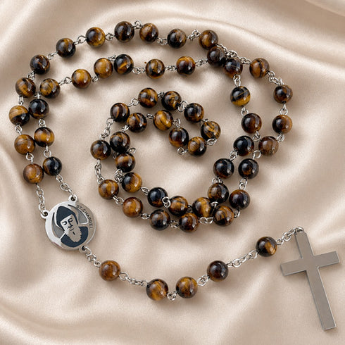 A rosary with brown tiger's eye beads, a round silver medal, and a silver cross, on a beige satin fabric background.