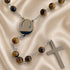 A rosary with polished brown tiger's eye beads, a round silver pendant with, and a flat silver cross.