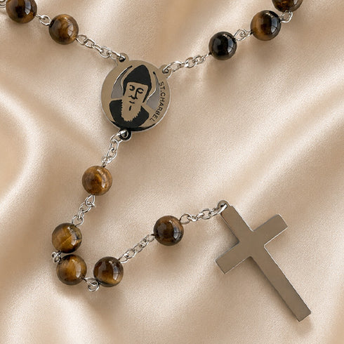 A rosary with brown tiger's eye beads, a St. Charbel medal, and a silver-tone cross, displayed on a satin background.