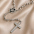 Stainless steel rosary close-up with circular St. Charbel medal and cross pendant on chain.