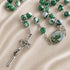 A close-up of a marbled green and white rosary laid on a beige satin fabric background.