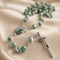 A green and white marbled rosary with a metal crucifix and oval centerpiece, on satin fabric.